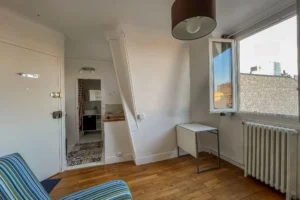 Pièce principale d’un appartement à Paris 15 avec parquet, fenêtre sur cour et coin cuisine aménagé, distribution optimisée autour de l’entrée et de la salle d’eau.