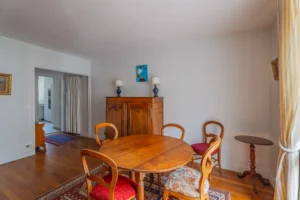 Salle à manger d’un appartement à vendre à Paris 12 Picpus, parquet ancien, table ronde en bois, chaises bistrot, buffet ancien, ouverture sur l’entrée et vue vers la cuisine, ambiance calme et chaleureuse.