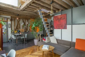 Salon avec cuisine ouverte, poutres apparentes et escalier menant à l’étage dans un appartement de caractère à Paris 10, secteur rue de Paradis / Faubourg Saint-Denis.