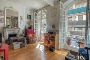 Vue du salon d’un appartement à Paris 17 Pont Cardinet avec parquet ancien, cheminée décorative, grandes portes-fenêtres et lumière naturelle.