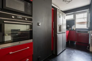 Cuisine moderne aménagée et équipée avec meubles rouges, four et micro-ondes encastrés, réfrigérateur américain et plan de travail sous fenêtre, appartement à Paris 12 secteur Dugommier Daumesnil.