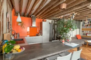 Cuisine ouverte avec îlot central, plan de travail contemporain, poutres apparentes et espace séjour dans un appartement à Paris 10, rue de Paradis.