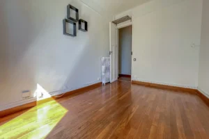Séjour vide avec parquet en bois, murs blancs, radiateur ancien et porte intérieure ouverte sur le dégagement, dans un appartement à Paris 12 Reuilly-Diderot.