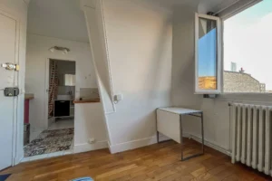 Pièce principale d’un appartement à Paris 15 avec parquet, coin cuisine intégré, fenêtre sur cour et agencement optimisé autour de l’entrée et de la salle d’eau.