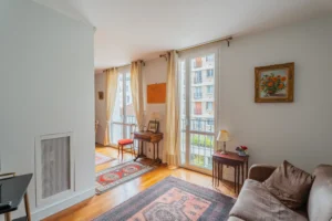 Vue du salon d’un appartement à vendre à Paris 12 Picpus, parquet en bois, canapé, tapis décoratif, grandes fenêtres, rideaux clairs et lumière naturelle apportant une atmosphère agréable.