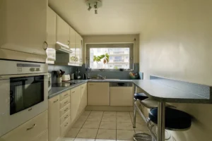 Cuisine équipée et lumineuse d’un appartement à vendre à Paris 12 Picpus, plan de travail en L, nombreux rangements, électroménager intégré et fenêtre donnant sur cour.