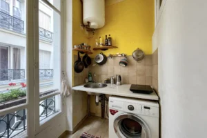 Petite cuisine de studio à Paris 10 avec fenêtre sur cour, évier et plaques de cuisson, rangements muraux, chauffe-eau et machine à laver, située rue du Faubourg Saint-Denis.