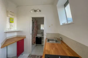 Espace cuisine d’un appartement à Paris 15 avec kitchenette fonctionnelle, plan de travail en bois, évier inox et accès direct à la salle d’eau.