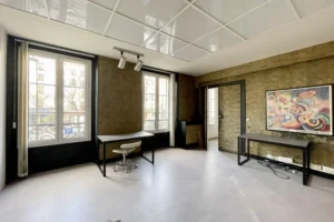 Salle à manger d’un appartement à vendre à Paris 11, secteur Filles du Calvaire / boulevard du Temple, avec grandes fenêtres, belle hauteur sous plafond et murs en pierre apparente.