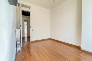 Séjour vide avec parquet en bois, murs blancs, radiateur ancien et porte intérieure ouverte donnant sur le dégagement, dans un appartement à Paris 12 Reuilly-Diderot.