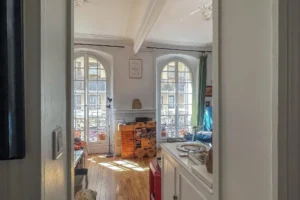 Vue du salon depuis l’entrée d’un appartement à Paris 17 Pont Cardinet, parquet ancien, volumes traversants et grandes fenêtres apportant une lumière naturelle.