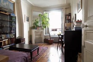 Chambre d’un appartement à Paris 5, quartier des Gobelins, avec parquet ancien, cheminée décorative, bibliothèque intégrée et belle luminosité grâce à une fenêtre