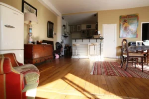 Espace repas et cuisine ouverte d’un appartement ancien à vendre à Paris 16 Molitor, parquet d’origine, coin bar avec tabourets, rangements et vue dégagée sur la pièce de vie.