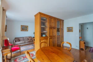 Pièce de vie d’un appartement à vendre à Paris 12 Picpus, parquet ancien, grande bibliothèque en bois faisant séparation, espace salon avec canapé et fauteuils, salle à manger attenante et circulation fluide entre les volumes.
