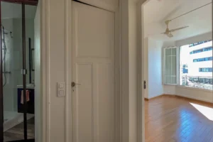 Vue depuis l’entrée d’un appartement avec parquet en bois, murs blancs et fenêtre laissant entrer la lumière, porte intérieure et salle d’eau visible en enfilade, à Paris 12 Reuilly-Diderot.