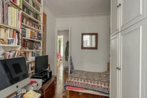 Chambre d’un appartement à Paris 17 Pont Cardinet avec parquet ancien, rangements intégrés, bibliothèque murale et ouverture sur le dégagement.