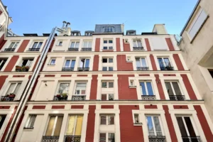 Façade intérieure d’un immeuble en briques rouges et encadrements clairs dans une cour à Paris 10, rue du Faubourg Saint-Denis, avec garde-corps en ferronnerie et ciel bleu.