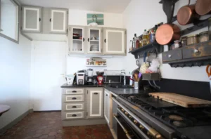 Cuisine indépendante d’un appartement ancien à vendre à Paris 16 Molitor, meubles de cuisine, plan de travail, four et piano de cuisson, étagères murales, carrelage au sol.