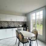 Cuisine lumineuse avec grande baie vitrée sur jardin, table repas et carrelage clair, maison à vendre à Saint-Benoît-d’Hébertot.