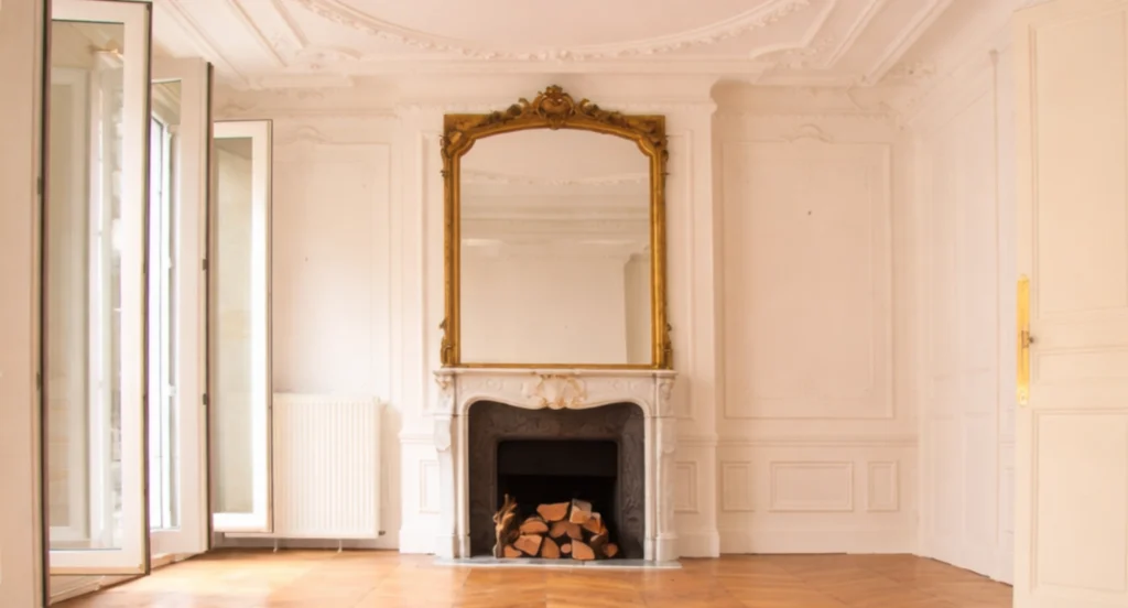 Salon haussmannien lumineux avec parquet en point de Hongrie, cheminée en marbre et moulures d’époque, illustrant l’équilibre et la justesse d’un lieu.