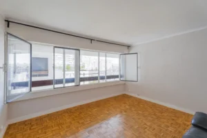 Séjour lumineux d’un appartement 2 pièces à Paris 12 Reuilly Diderot avec grande baie vitrée, vue dégagée sur les immeubles environnants et parquet mosaïque au sol.