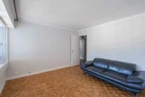 Séjour d’un appartement 2 pièces à Paris 12 Reuilly Diderot avec parquet mosaïque, murs blancs, canapé et accès vers le dégagement nuit.