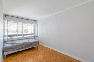 Chambre lumineuse d’un appartement 2 pièces à Paris 12 Reuilly Diderot avec parquet mosaïque, grande fenêtre et vue dégagée sur les immeubles environnants.