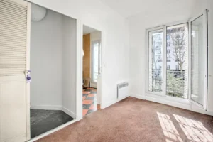 Salle de bains avec baignoire, fenêtre et WC, carrelage beige et sol damier, appartement en duplex à vendre Paris 12 Porte de Vincennes Avenue Saint-Mandé.