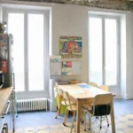 Cuisine avec coin repas et table familiale, deux grandes fenêtres apportant une forte luminosité, sol en carreaux anciens, ambiance conviviale et fonctionnelle, appartement Paris 2 Sentier rue de Tracy.