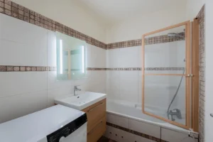 Salle de bains avec baignoire, meuble vasque en bois et miroir lumineux dans un appartement 2 pièces à Paris 12 Reuilly Diderot.