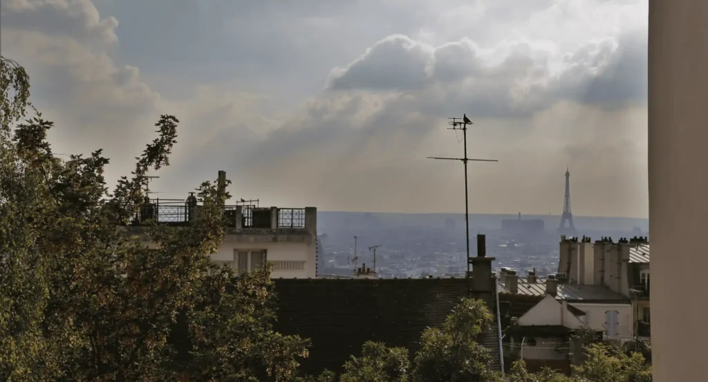 Vue sur la Tour Eiffel depuis Montmartre avec toits parisiens et végétation au premier plan dans le 18e arrondissement de Paris