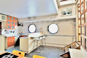 Cuisine ouverte d’une péniche avec comptoir bar et deux hublots donnant sur la Seine à Levallois-Perret quai Charles Pasqua.