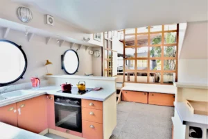 Cuisine fonctionnelle d’une péniche avec plan de travail, four intégré et hublots ronds laissant entrer la lumière naturelle à Levallois-Perret quai Charles Pasqua.