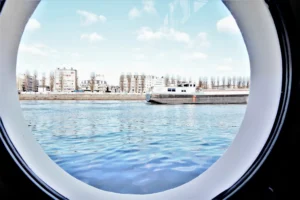 Vue sur la Seine et les immeubles de Levallois-Perret à travers un hublot rond d’une péniche amarrée quai Charles Pasqua.