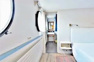 Chambre d’une péniche avec hublot et accès direct à une salle d’eau située à Levallois-Perret quai Charles Pasqua.