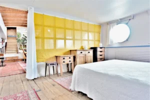 Chambre spacieuse d’une péniche avec parquet ancien, hublot rond et mobilier en bois située à Levallois-Perret quai Charles Pasqua.