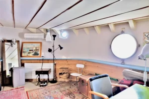 Espace bureau aménagé dans une péniche avec hublot rond, plafond bas et coin lecture à Levallois-Perret quai Charles Pasqua.