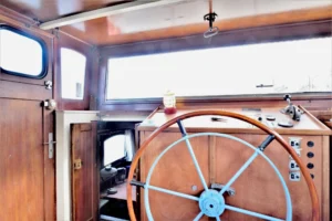 Poste de pilotage d’une péniche avec grande barre de gouvernail en bois et timonerie intérieure offrant une vue sur la Seine à Levallois-Perret.