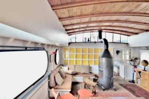 Salon chaleureux d’une péniche aménagée avec plafond voûté en bois, poêle à bois central et banquette intégrée à Levallois-Perret quai Charles Pasqua.