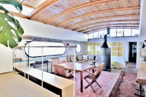 Séjour lumineux d’une péniche avec plafond voûté en bois, grande table à manger et poêle central, aménagé en espace de vie ouvert à Levallois-Perret quai Charles Pasqua.