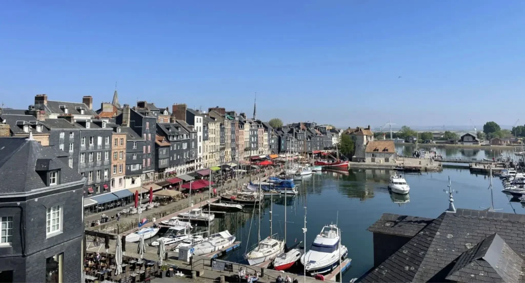 Vue panoramique du Vieux Bassin de Honfleur avec ses maisons étroites colorées, ses bateaux de plaisance et les quais animés du port historique.