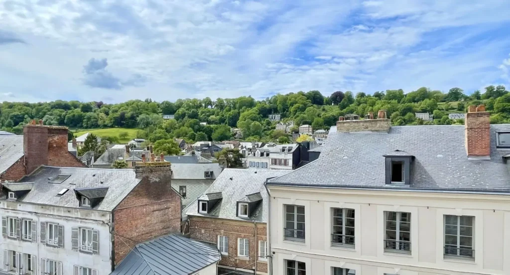 Vue sur les toits du centre historique de Honfleur avec les maisons anciennes et les collines verdoyantes de la Côte de Grâce en arrière-plan, en Normandie.